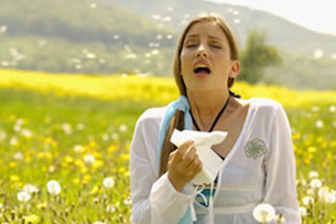 Young woman in a field of wildflowers holding a tissue and sneezing